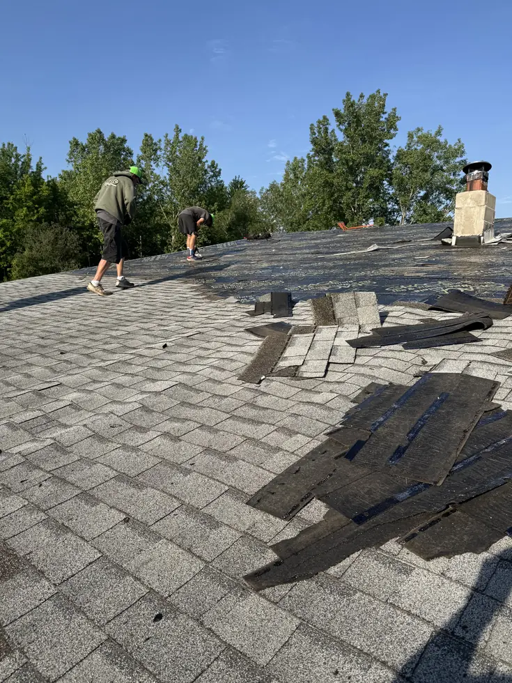Roof tear-off in progress with old shingles being stripped to the deck