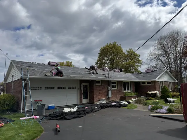 Roof replacement underway on a brick ranch home with materials staged in the driveway