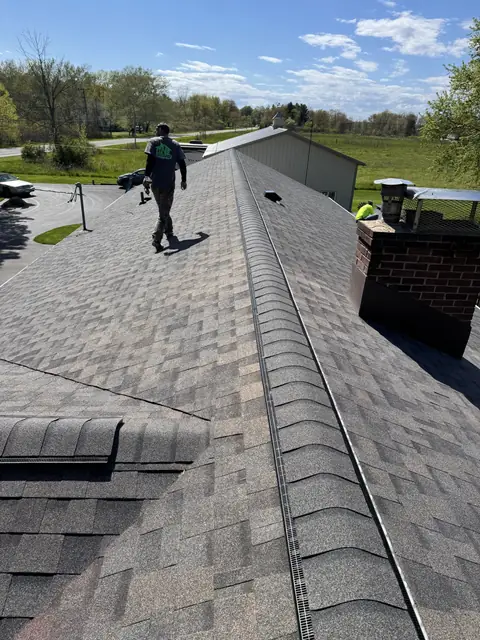 A TNE roofer walking the ridge of a newly finished shingle roof